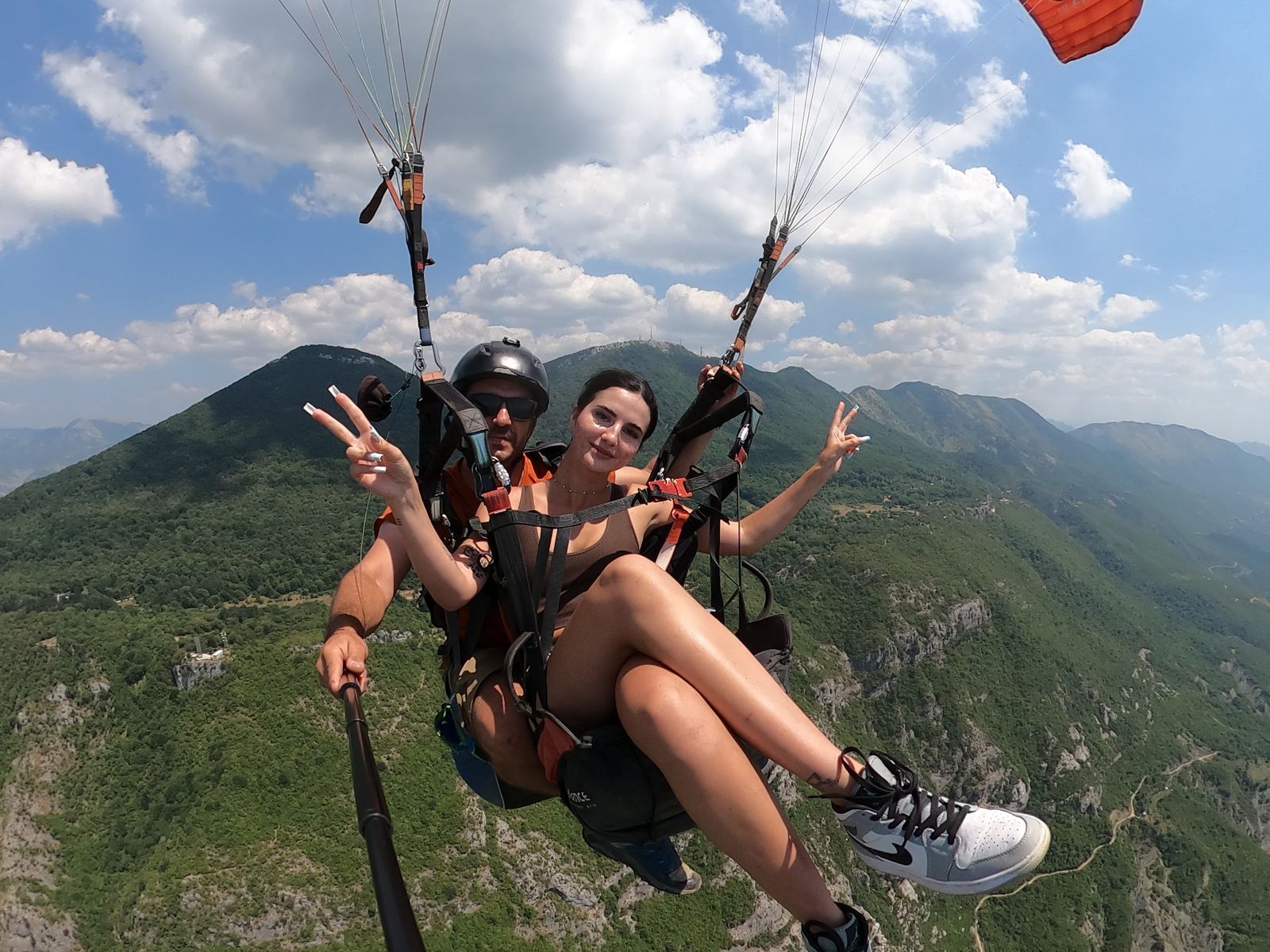 Passenger throwing peace signs under towering cumulus, the Dajti summit antenna visible on the ridge behind.